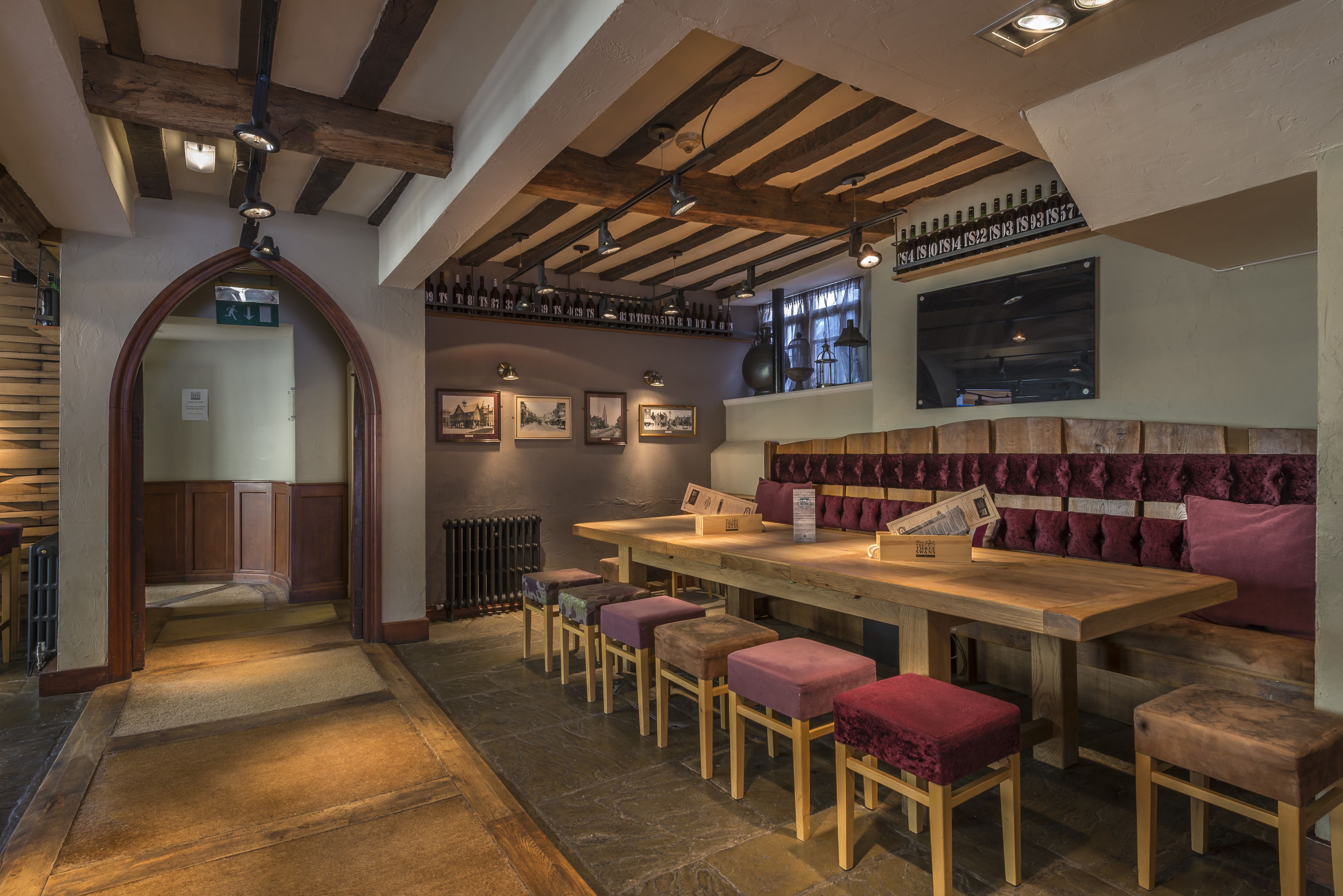 Ein Restaurant mit Holztischen und gepolsterten Barhocker, einer hohen Decke mit freiliegenden Balken und gerahmten Bildern an den Wänden.