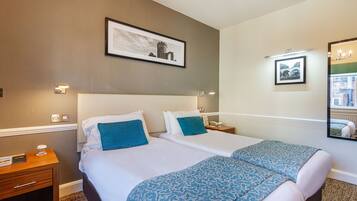 A hotel room with two beds, a nightstand, a framed picture on the wall, and a mirror.