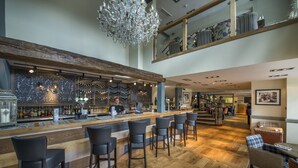 A bar area with a wooden counter, multiple bar stools, and a chandelier. - The Three Swans Hotel, Market Harborough, Leicestershire (Market Harborough)