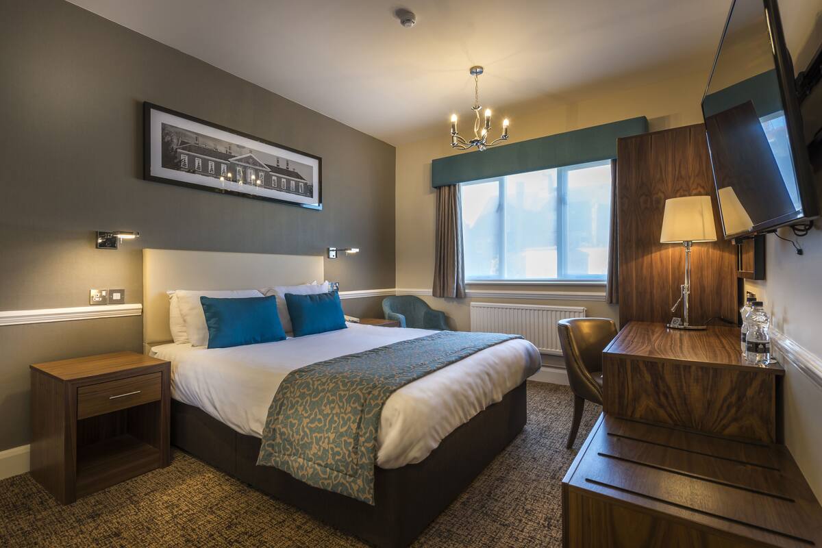 A hotel room with a large bed, a desk, a chair, a framed picture on the wall, and a window with curtains.