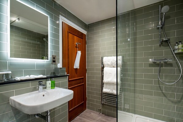 A modern bathroom with a glass shower enclosure, a wooden door, and a white sink with a mirror above it. - The Three Swans Hotel, Market Harborough, Leicestershire (Market Harborough)