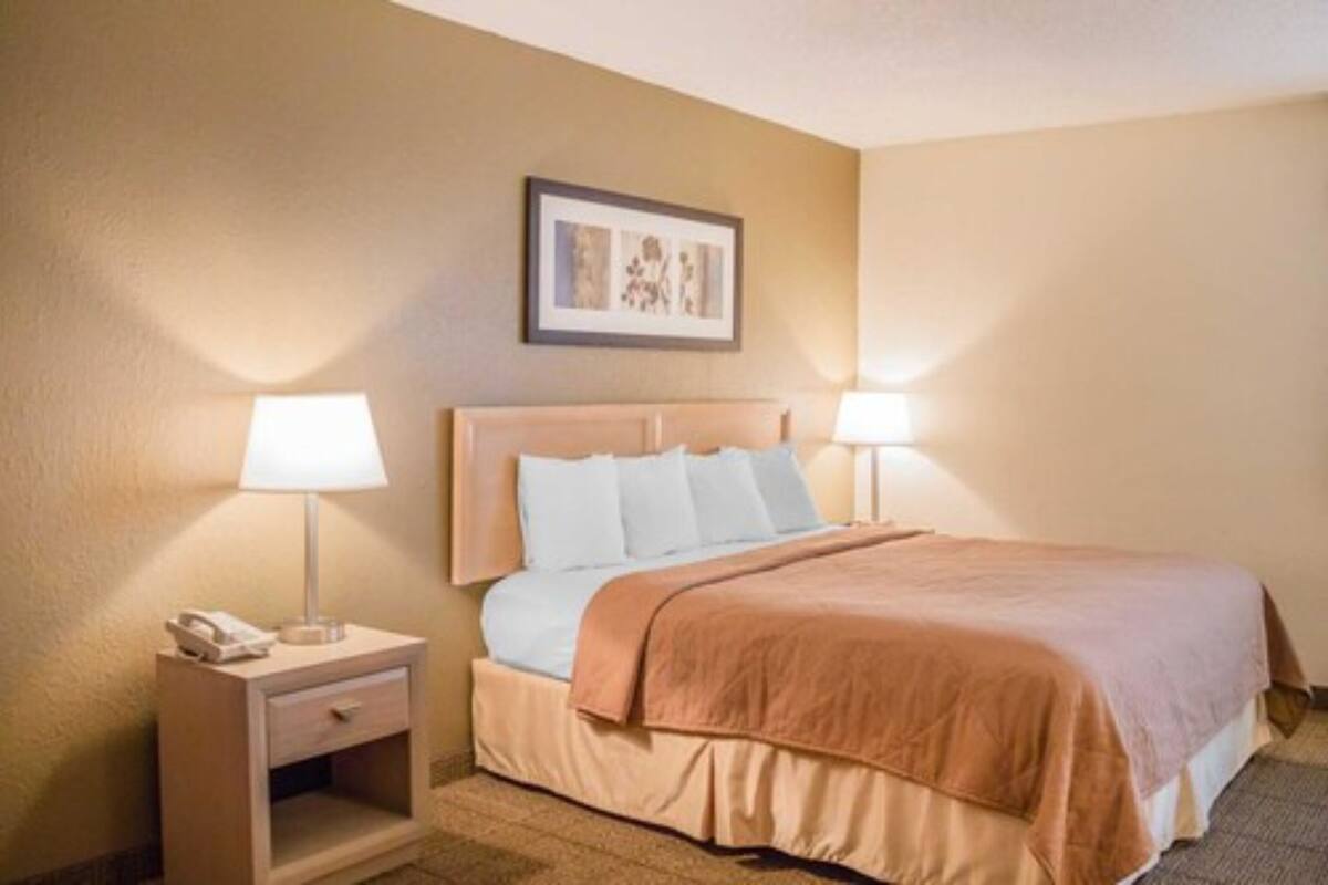 Une chambre d’hôtel avec un lit, des lampes de chevet, une table de nuit et un tableau encadré au mur.