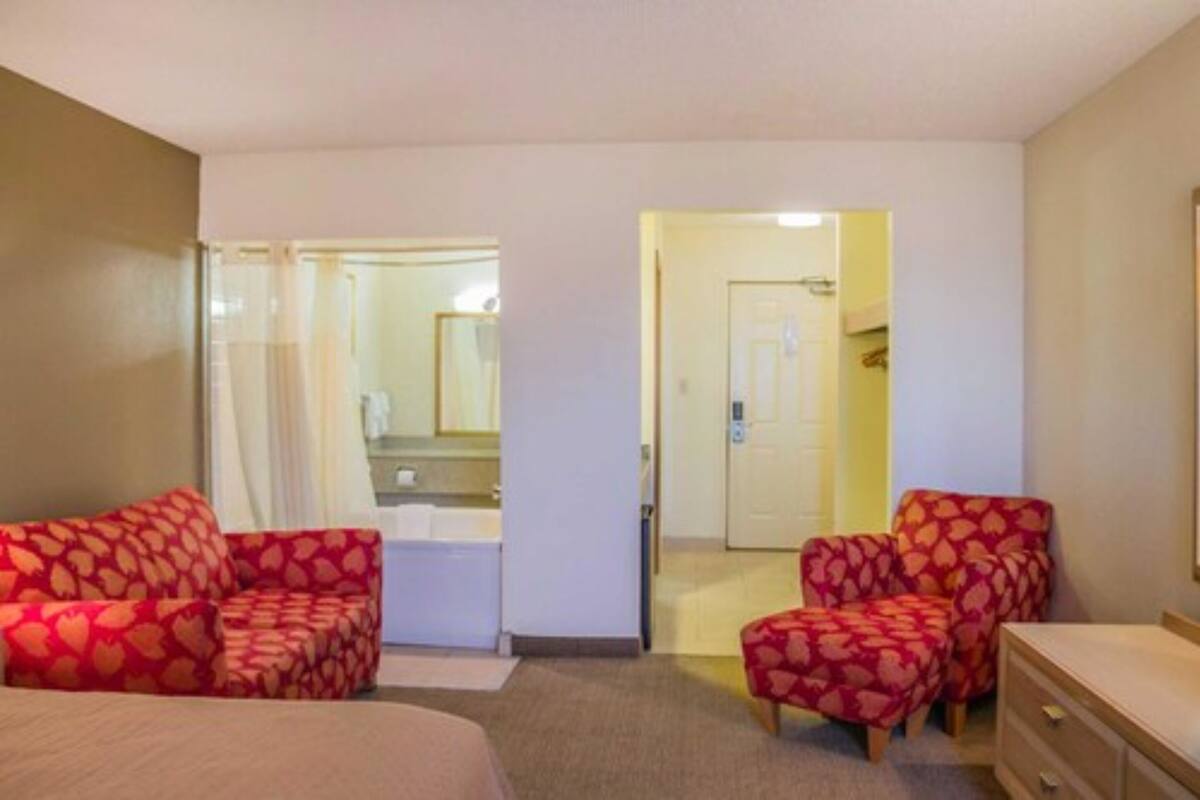 Une chambre d’hôtel comprenant un lit, deux fauteuils, une commode et une porte donnant sur une salle de bain.