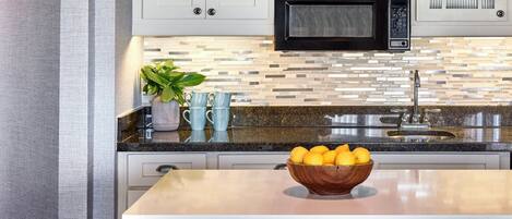 A kitchen with a microwave, a sink, a bowl of lemons, and a plant on the counter.