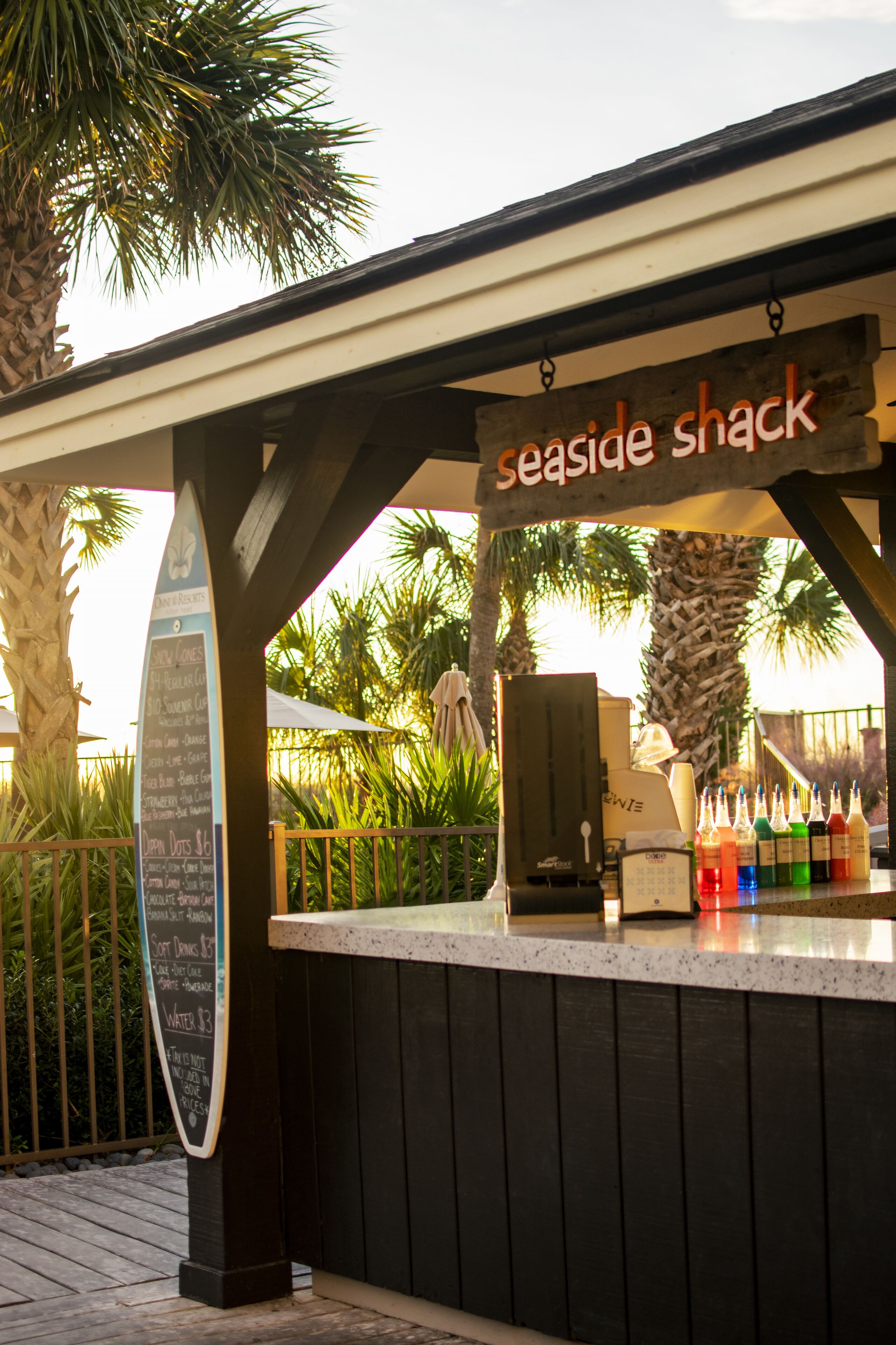 A seaside shack with a menu board, a cash register, and a variety of drinks displayed.