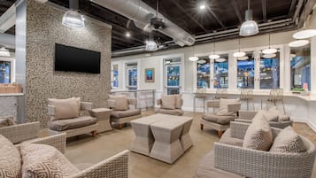 Un amplio salón con mobiliario de mimbre, un televisor de pantalla plana y ventanas grandes con vistas a la ciudad.