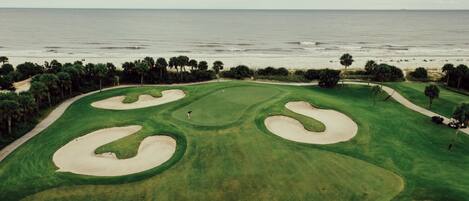 A golf course with sand bunkers and a view of the ocean.