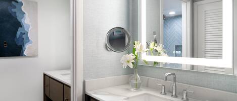 Une salle de bain moderne avec un grand miroir, un lavabo blanc et un vase rempli de fleurs blanches.