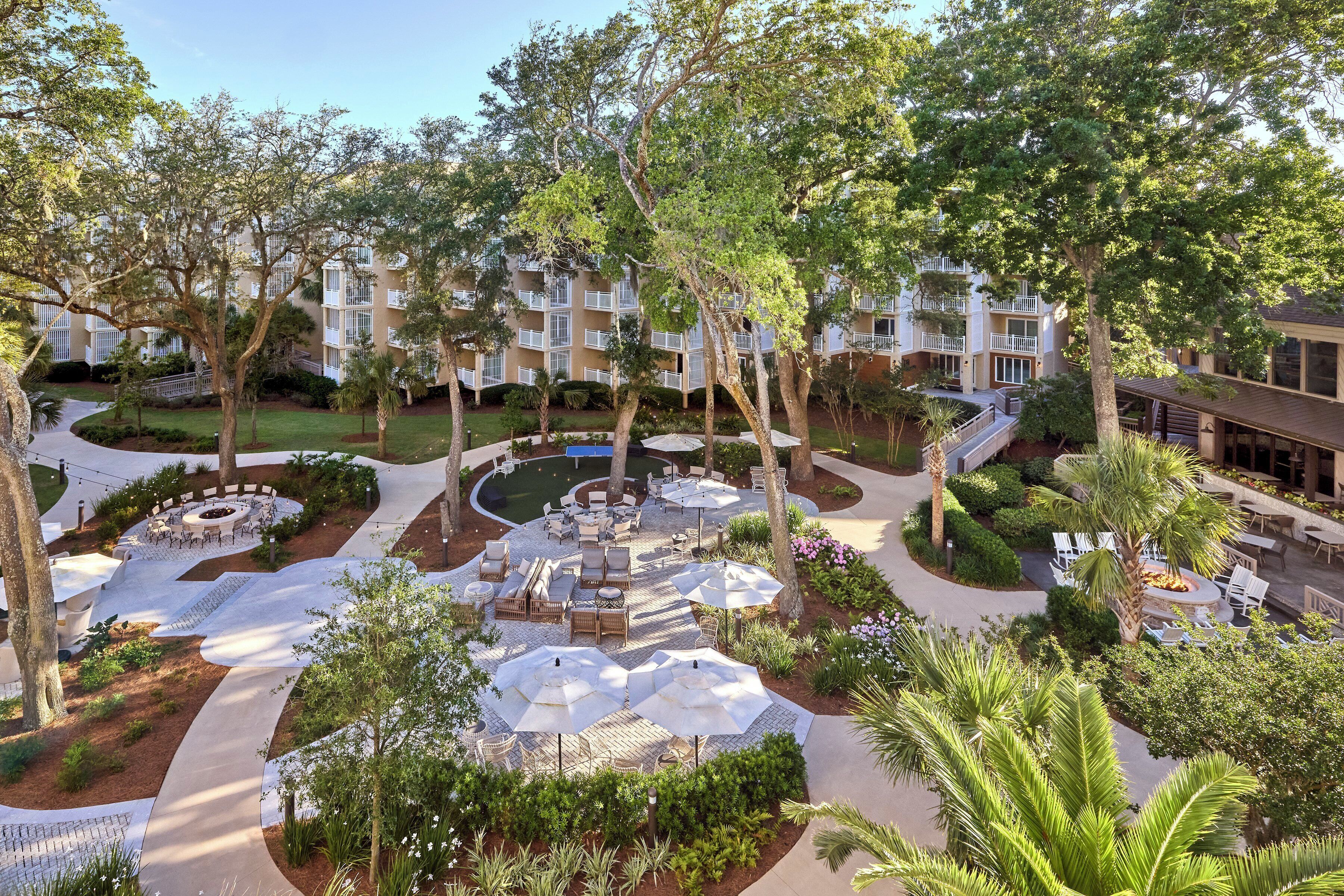 A resort with a central courtyard featuring outdoor seating, a circular fire pit, and surrounding greenery.