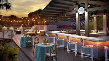 Un espace extérieur aménagé en terrasse, avec des tables et des chaises rondes, un bar et des guirlandes lumineuses.