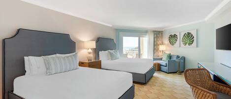 A hotel room with two beds, a desk, a chair, and a balcony with a view.