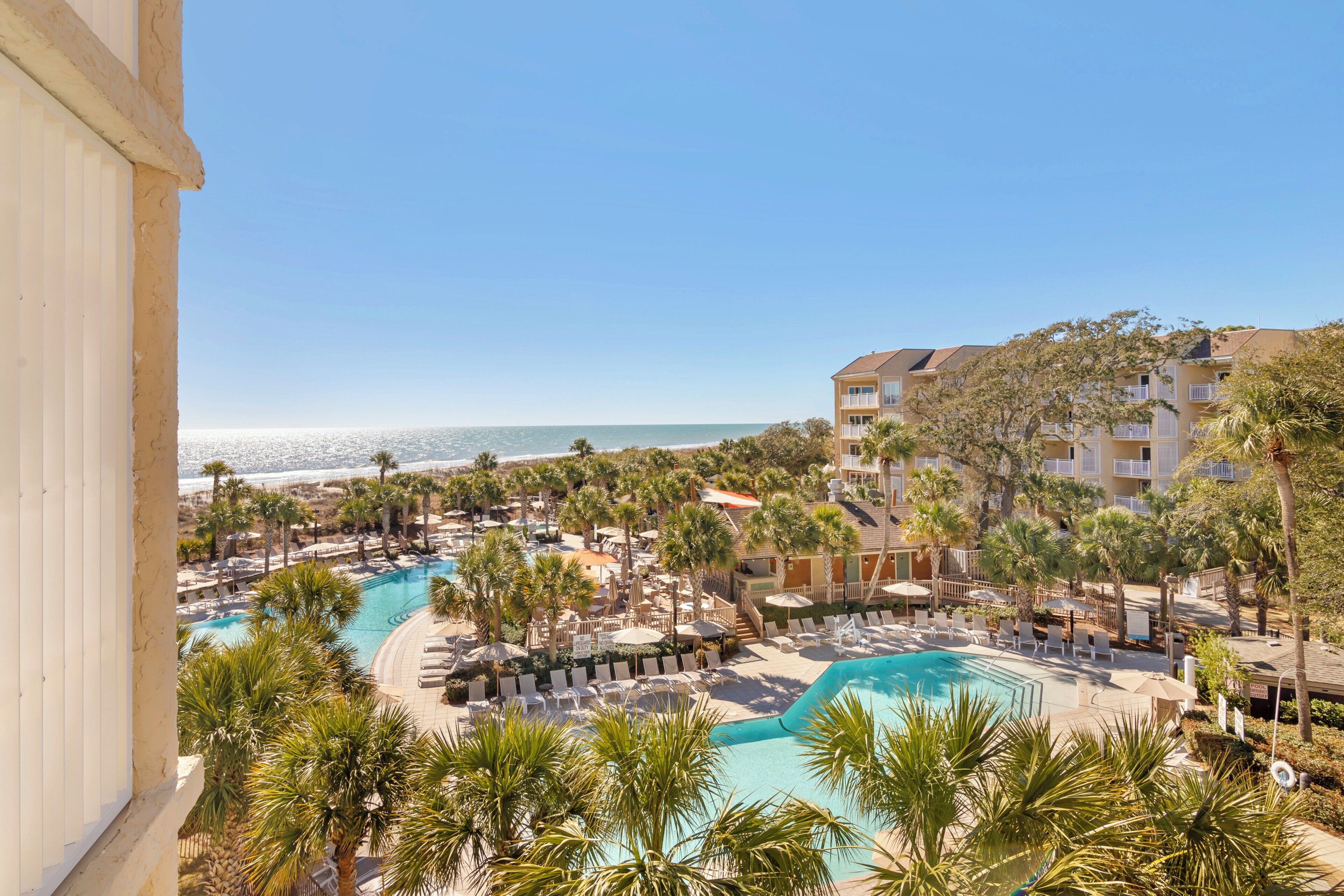Un complexe hôtelier doté d’une piscine, de palmiers et offrant une vue sur la plage.