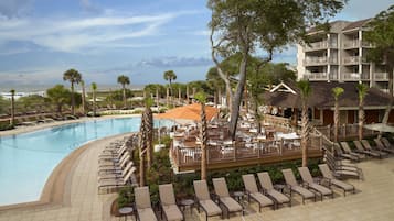 A resort pool area with lounge chairs and umbrellas, overlooking a beach and ocean.
