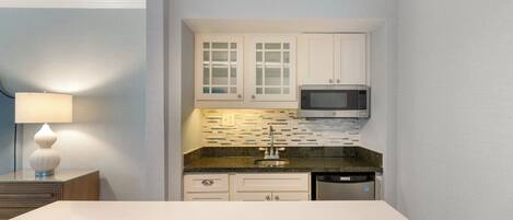 Una cocina compacta con muebles blancos, un microondas y un lavavajillas.