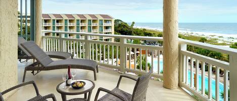 A balcony with wicker furniture, a table with a bowl and wine glasses, and a view of the ocean and beach.