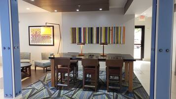 A modern hotel lobby with a conference table, chairs, a patterned rug, a wall art piece, and a colorful striped wall decoration.