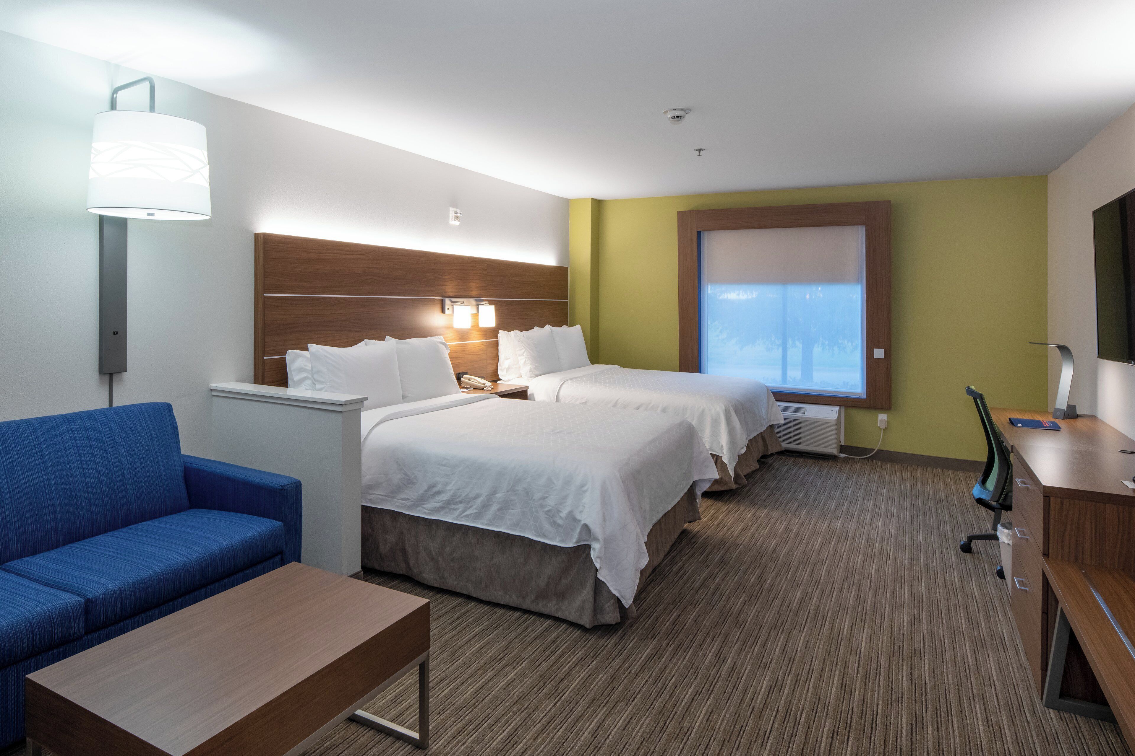 A hotel room with a bed, a desk, a chair, a sofa, and a window.
