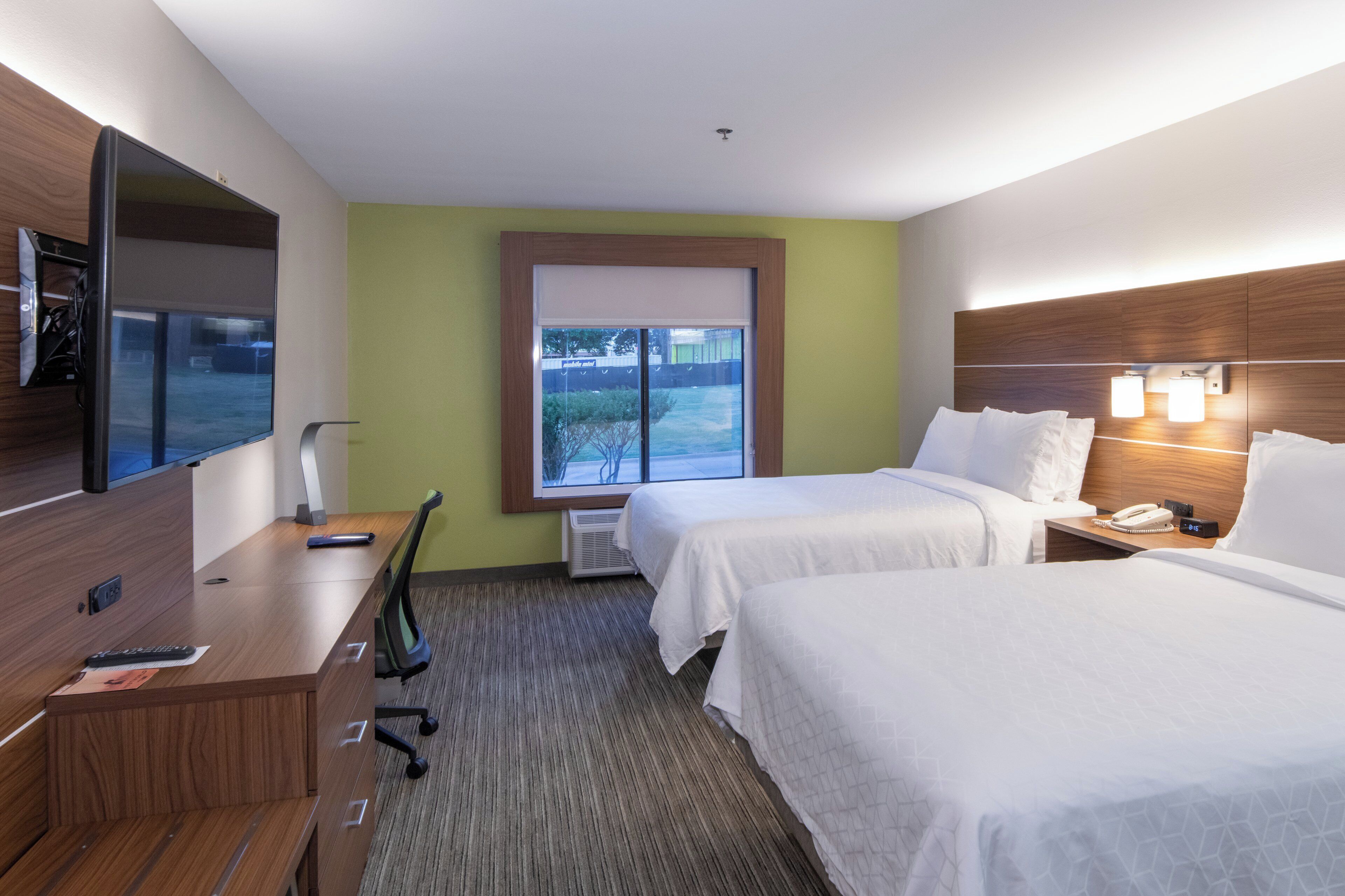 A hotel room with two beds, a desk with a chair, a television, and a window with a view of the outdoors.