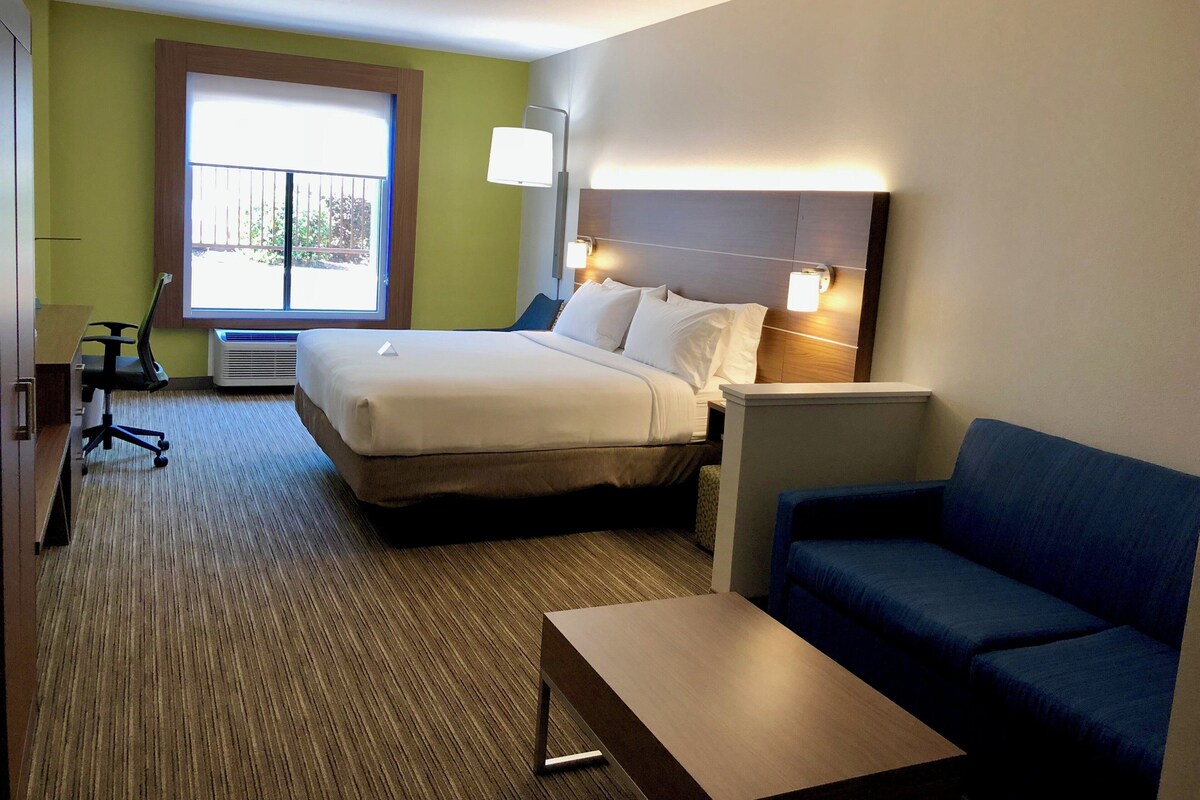 A hotel room with a bed, a desk, a chair, a sofa, and a window with a view.