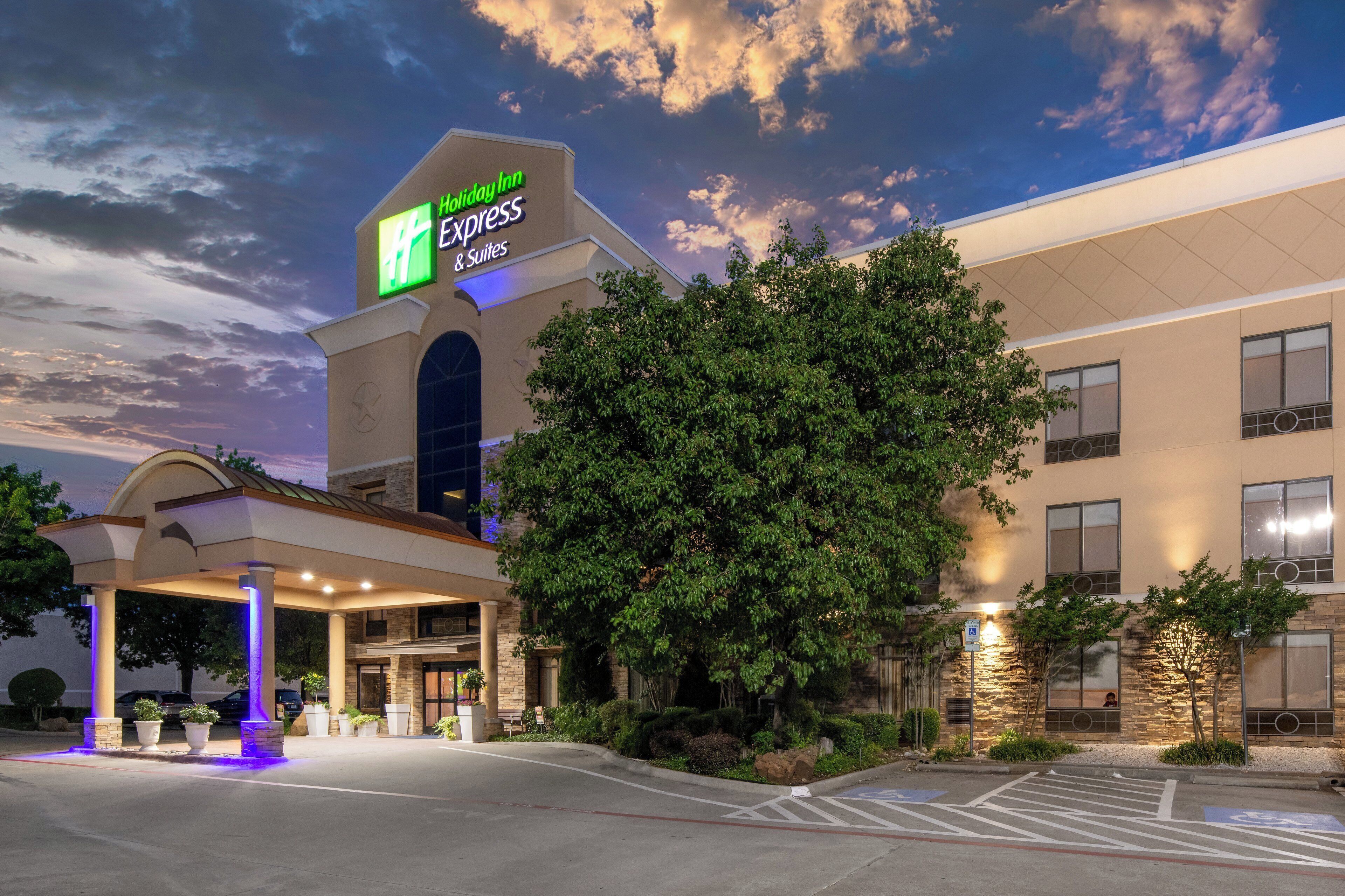 A Holiday Inn Express & Suites hotel with a large tree in front, a covered entrance, and a parking lot.