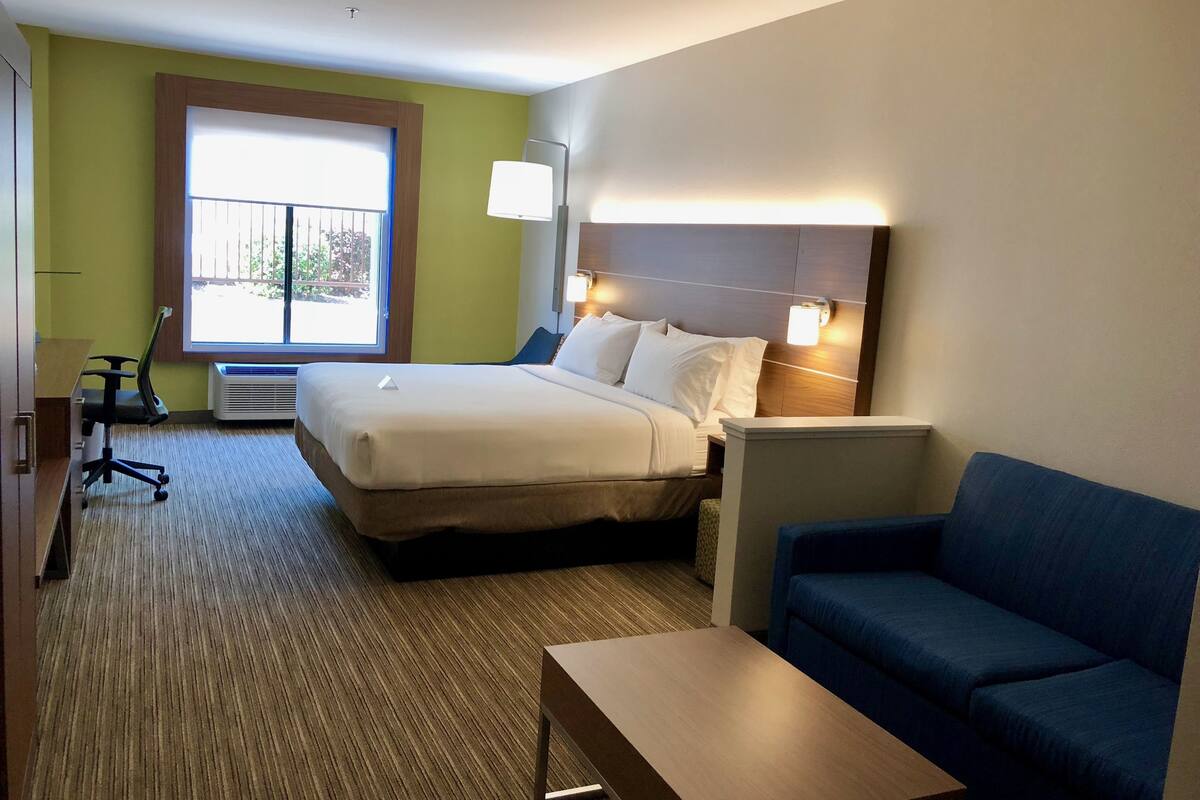 A hotel room with a bed, a desk, a chair, a sofa, and a window with a view of the outdoors.