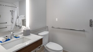 A bathroom with a white sink, mirror, and toilet. There are handrails on the walls and a towel rack.