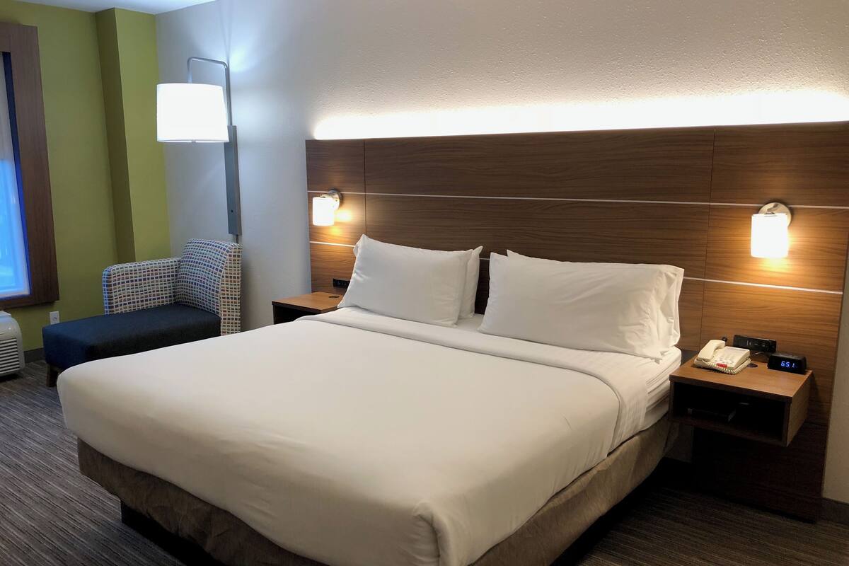 A hotel room with a large bed, two bedside tables, a chair, and a wall-mounted lamp.