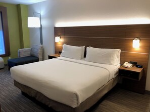 A hotel room with a large bed, two bedside tables, a chair, and a wall-mounted lamp.