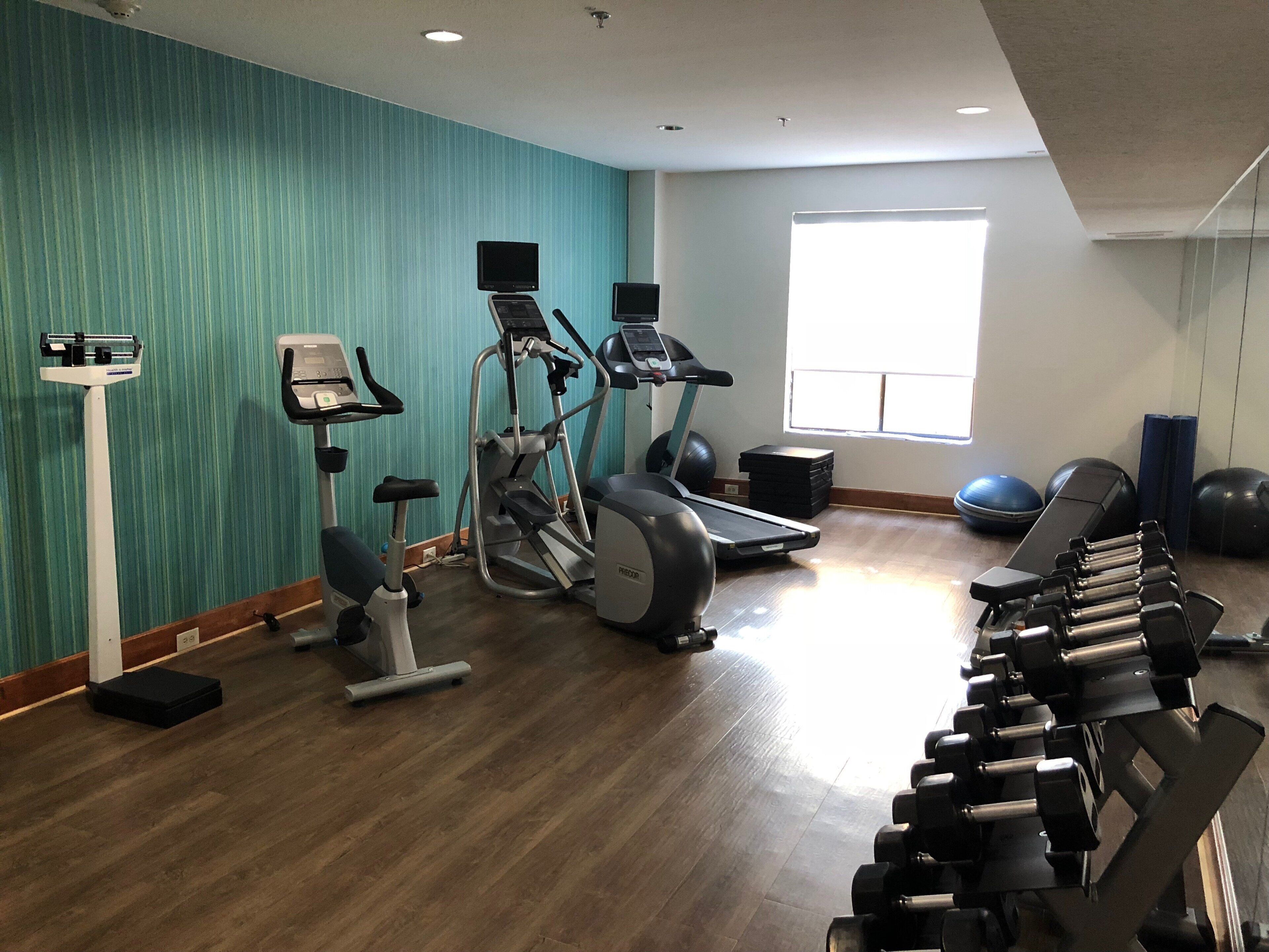 A gym with exercise equipment, a standing bike, and a window providing natural light.