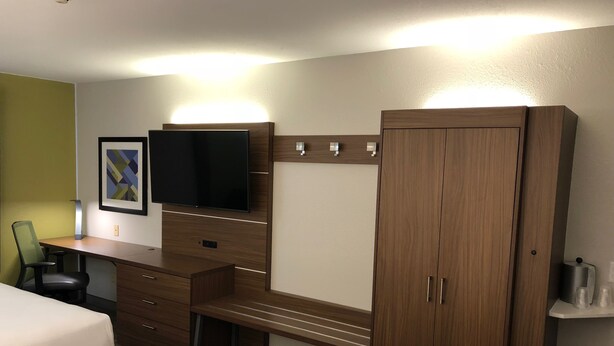 A hotel room with a bed, a desk with a flat-screen TV, a wardrobe, and a chair.