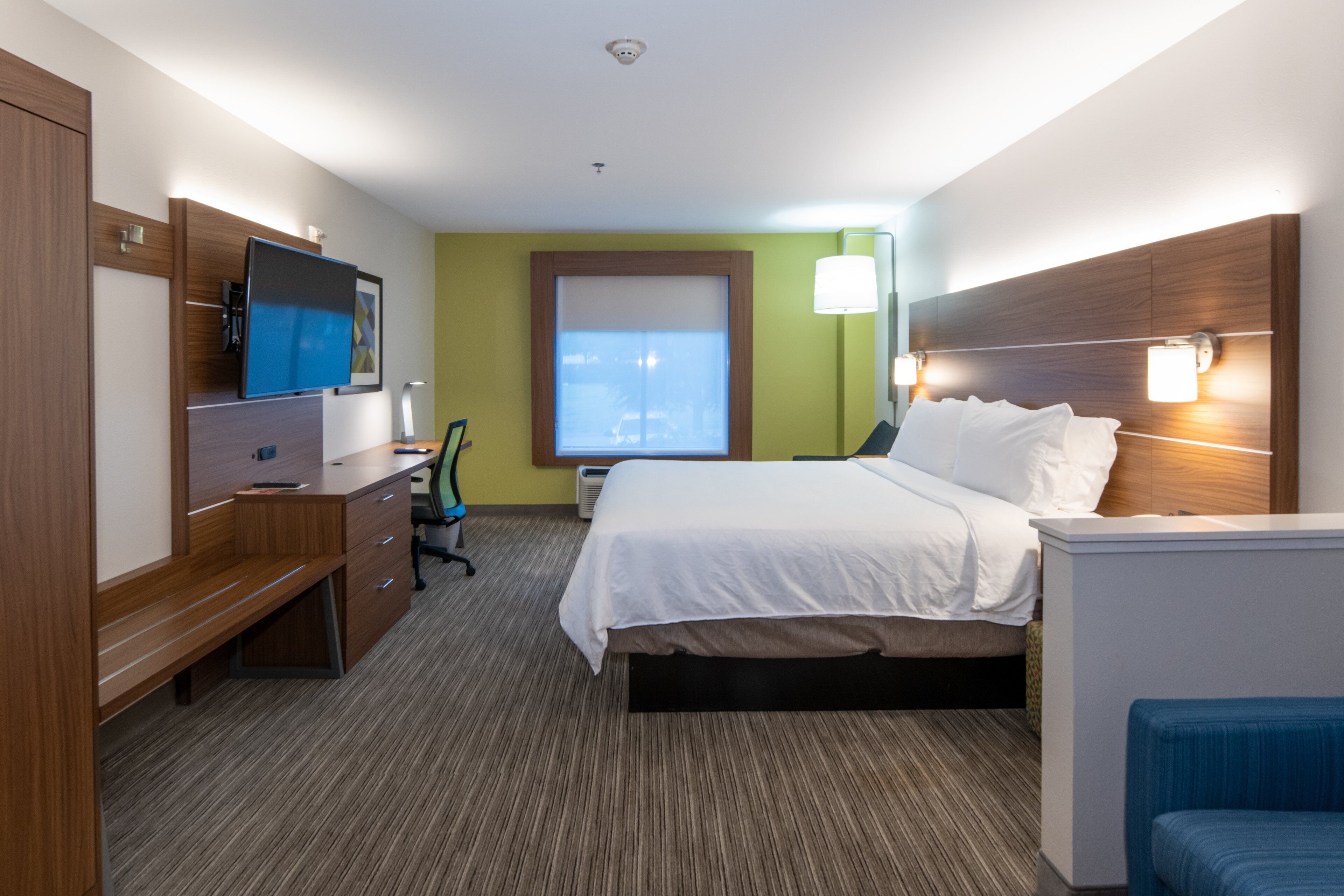 A hotel room with a bed, desk, chair, TV, and a window with blinds.