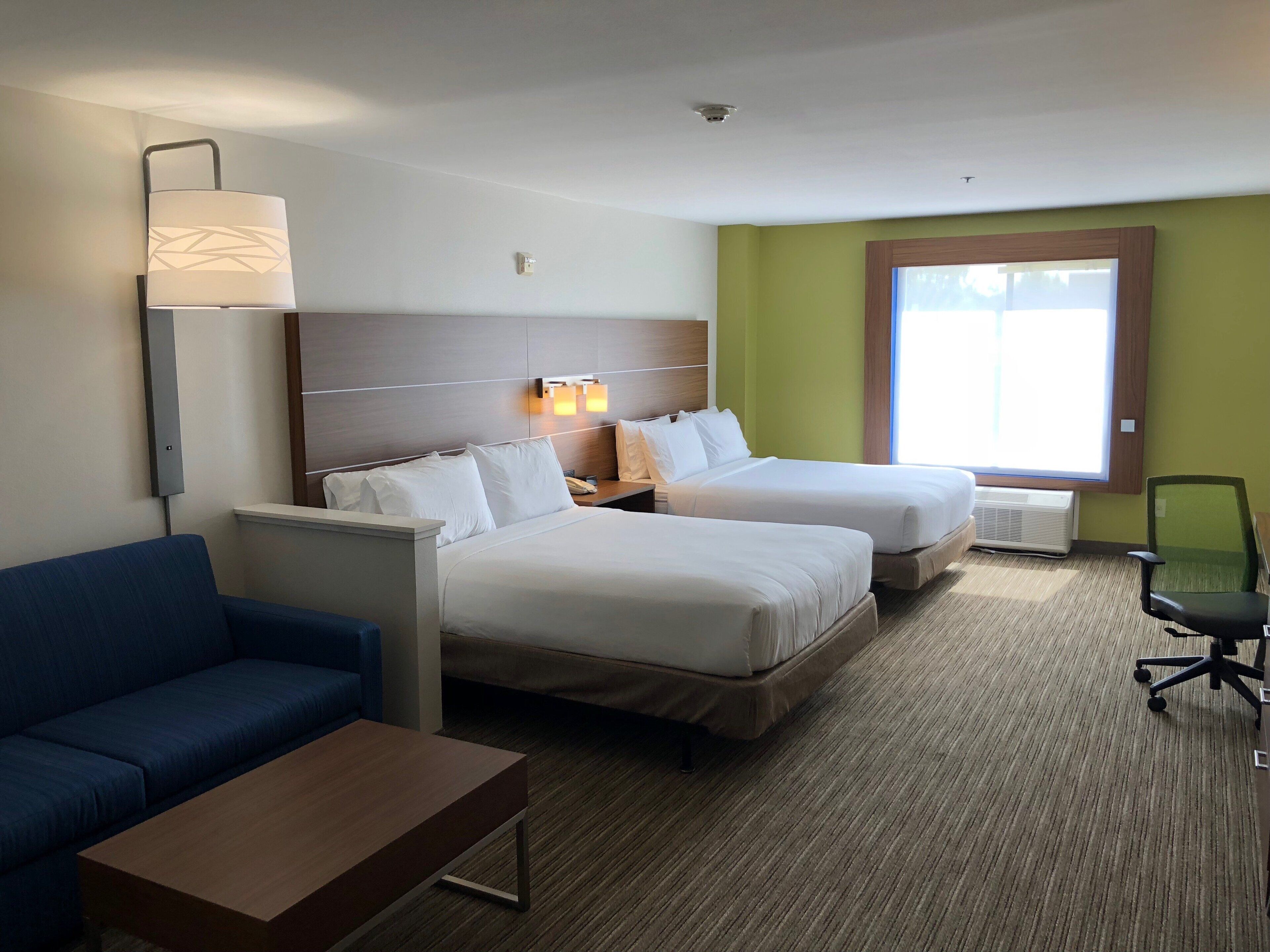 A hotel room with two beds, a desk, a blue sofa, and a window with a view.