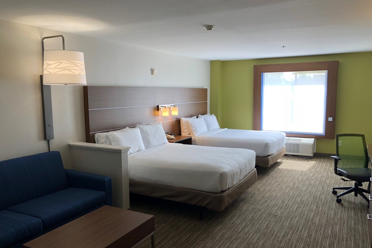A hotel room with two beds, a desk, a blue sofa, and a window with a view.