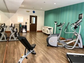 A fitness center with various exercise equipment, including treadmills and weight machines, and a sign indicating the location.
