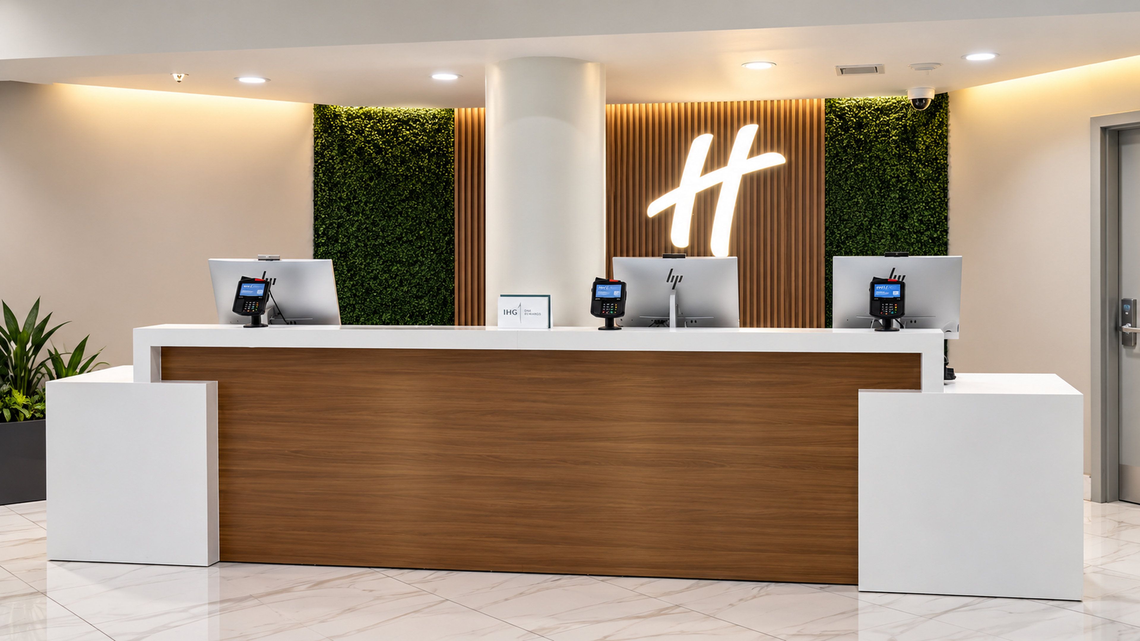 A reception desk with a wooden panel, two computer monitors, and a large illuminated 'H' sign.