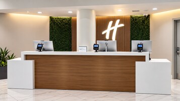 A reception desk with a wooden panel, two computer monitors, and a large illuminated 'H' sign.