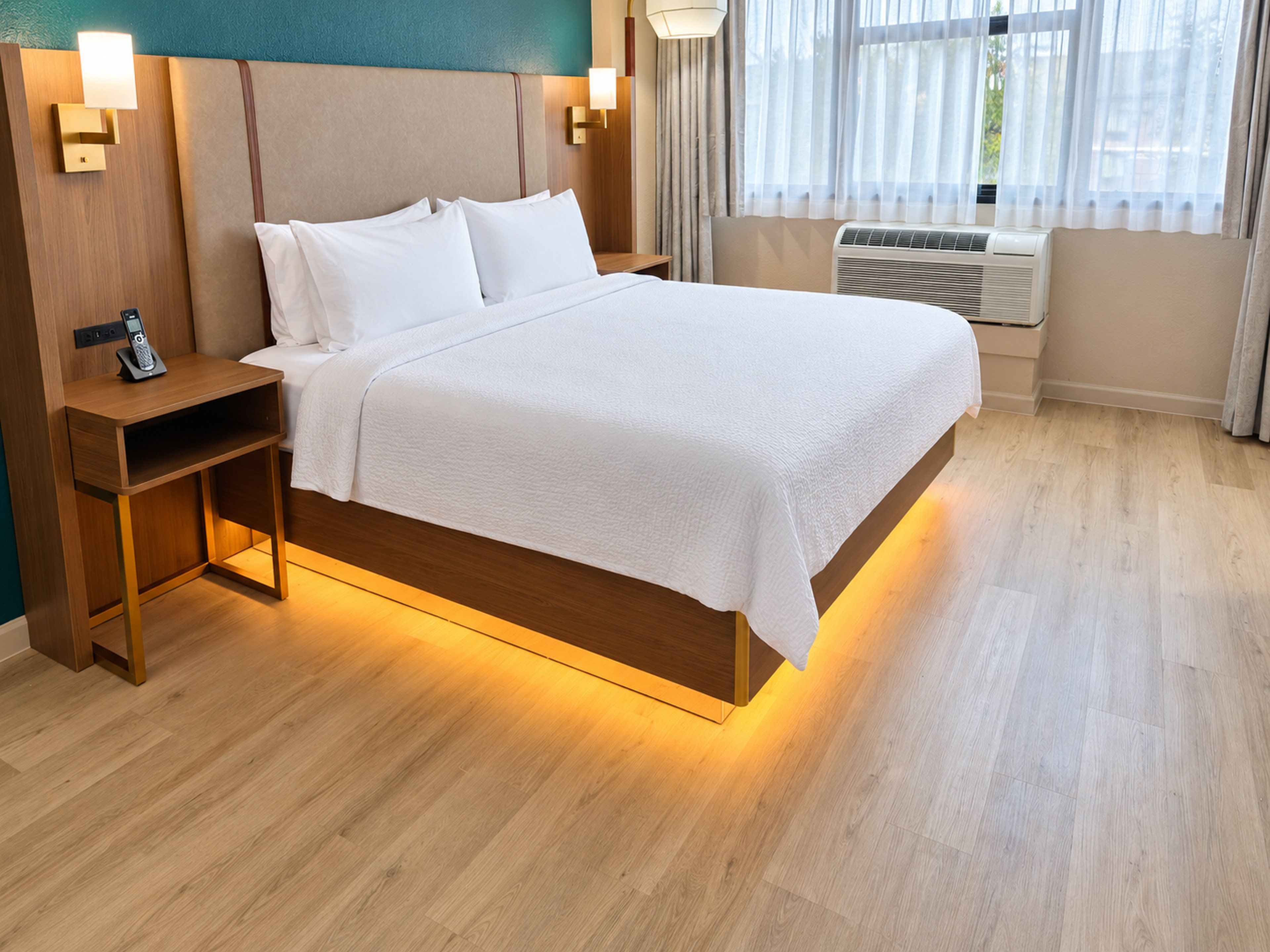 A hotel room with a bed, bedside tables, a telephone, and an air conditioning unit.