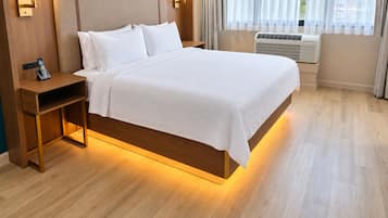 A hotel room with a bed, bedside tables, a telephone, and an air conditioning unit.