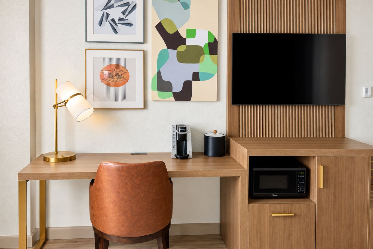 A modern kitchen with a wooden countertop, a black microwave, a coffee maker, and a television mounted above the counter.