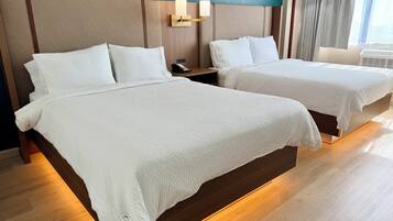 Deux lits avec du linge de lit blanc, une table de chevet avec un téléphone et un luminaire fixé au mur.