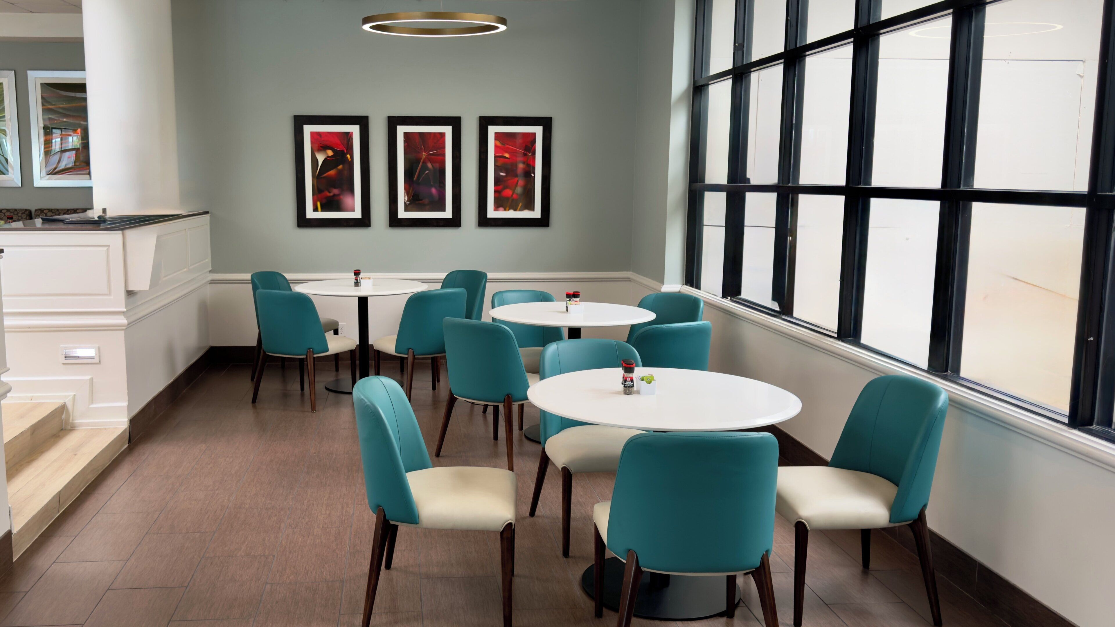 A dining area with teal chairs, white tables, and framed artwork on the wall.