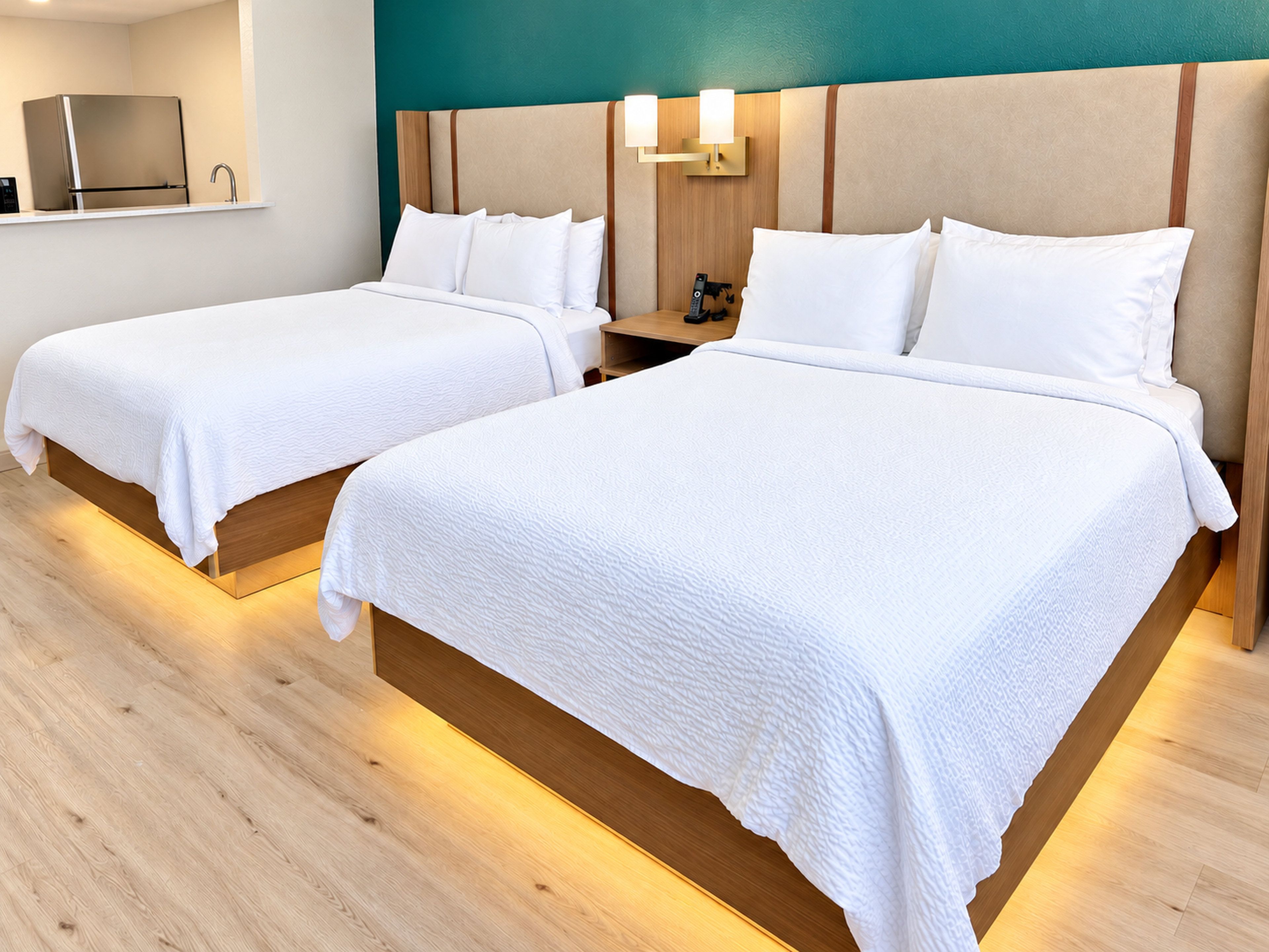 Two single beds with wooden headboards and white bedding, a nightstand with a lamp, and a television on a shelf above the beds.