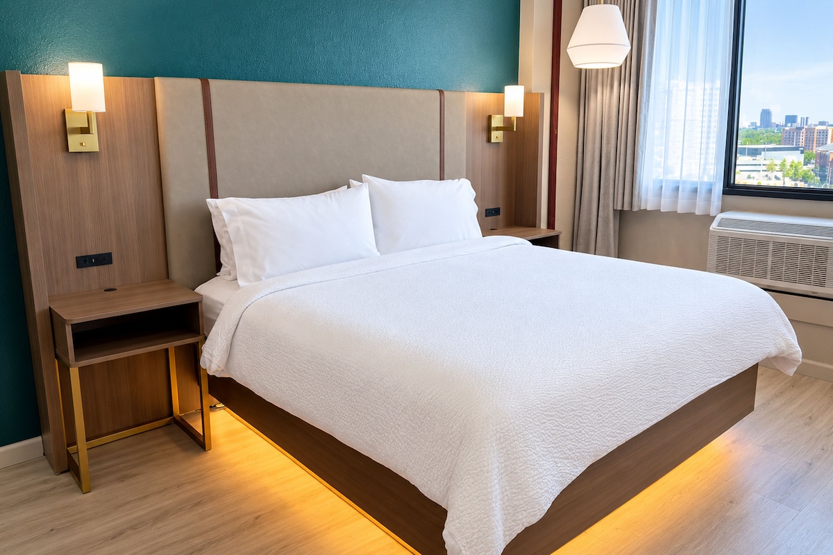 A hotel room with a large bed, bedside tables, and a view of the city through the window.