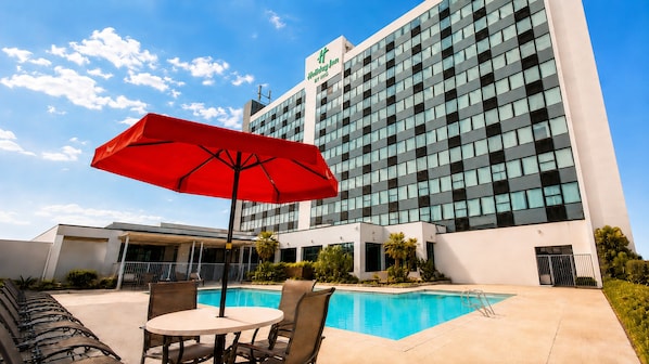 A hotel with a swimming pool, outdoor seating, and a red umbrella.