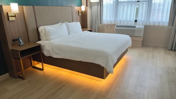 Una habitación de hotel con cama, mesita de noche, lámpara y aire acondicionado.