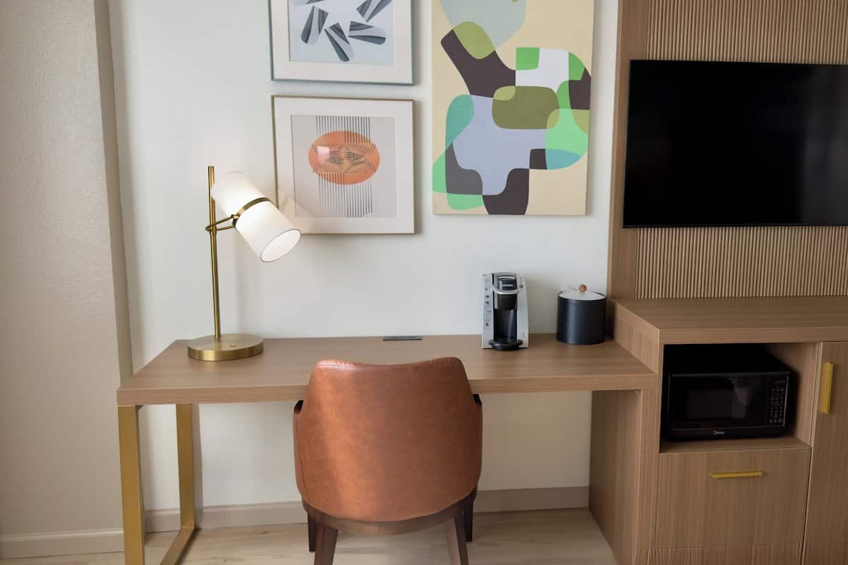 A modern office space with a wooden desk, a leather chair, a coffee maker, a TV, and abstract art on the wall.