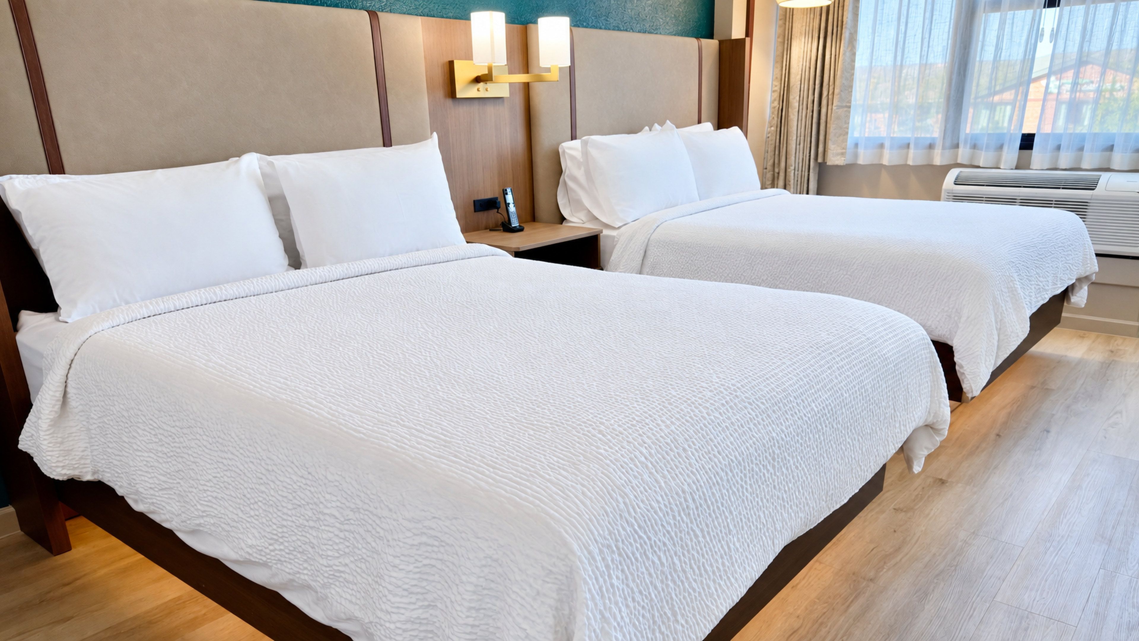 Une chambre d’hôtel avec deux lits, une table de chevet avec un téléphone et une fenêtre avec des rideaux.