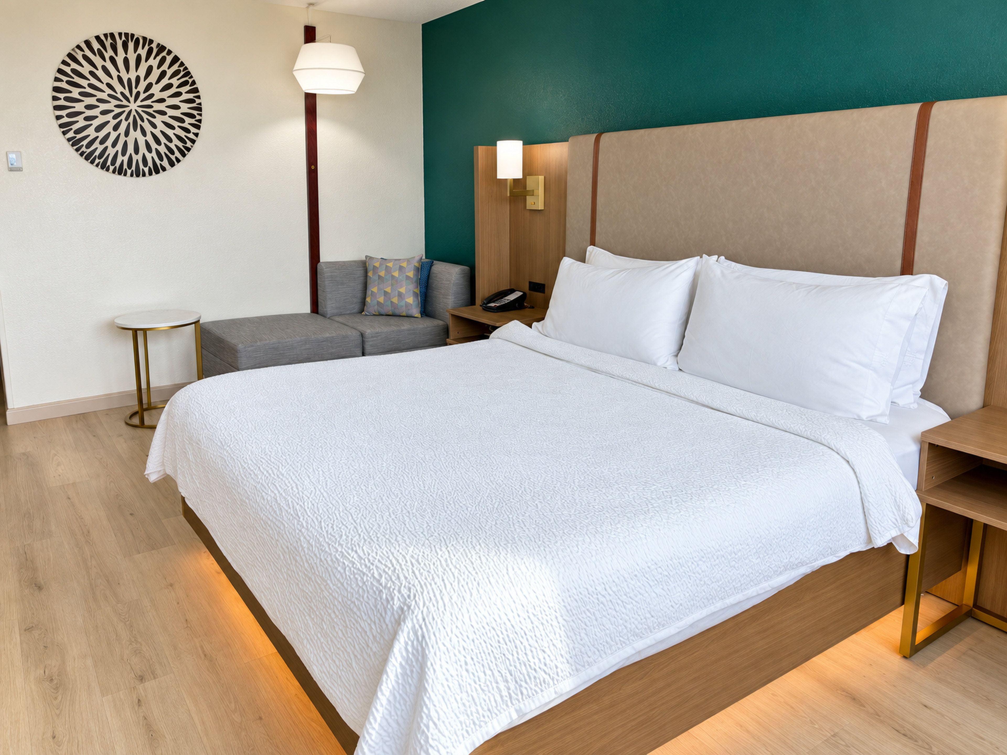 Une chambre d’hôtel avec un grand lit, une table de chevet, une lampe, une œuvre d’art murale et un petit coin salon.