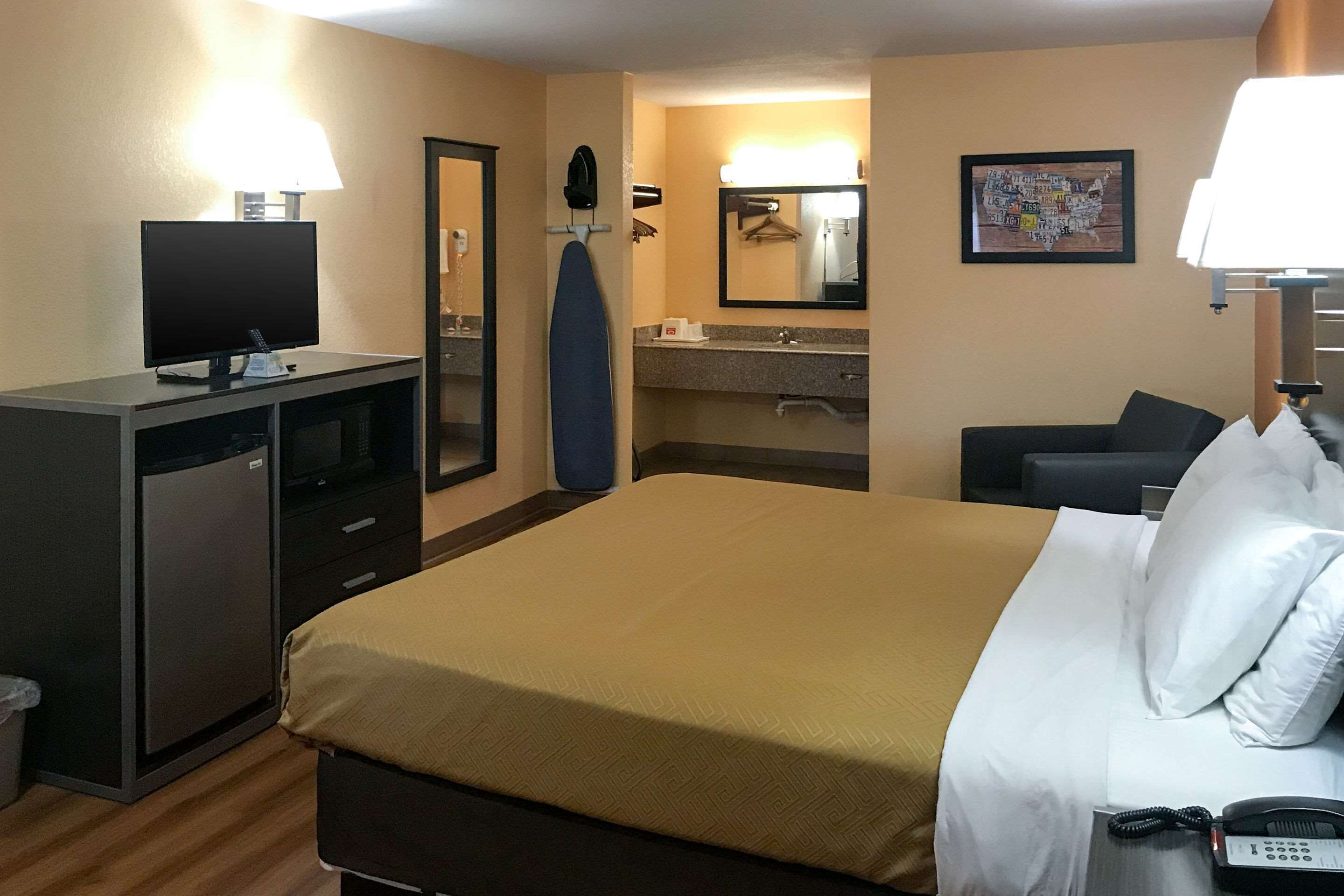 A hotel room with a bed, desk, TV, and a bathroom with a mirror and towel rack.
