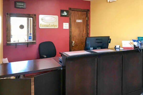 Un mostrador de recepción con una computadora, una silla, una ventana y una puerta con la leyenda 'Solo personal'.